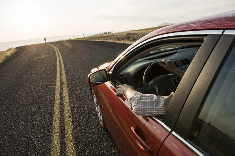 An automobile approaching a person standing on the side of a road.