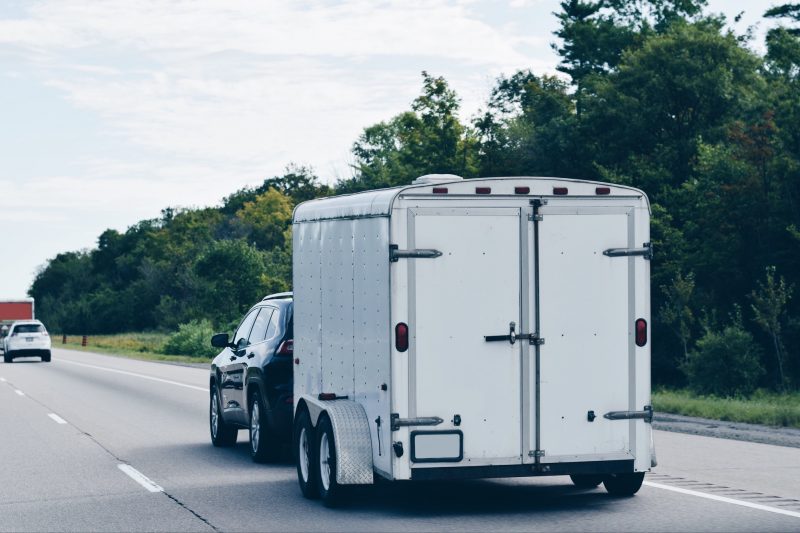 Trailer attached to a car driving on a highway carrying furniture and personal belongings